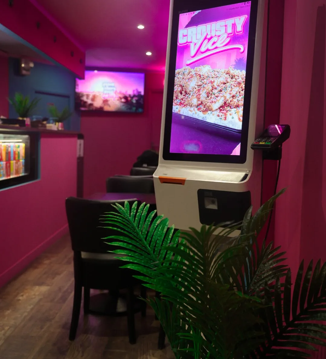 Une borne de commande tactile Crousty Vice sous les néons roses, avec son terminal de paiement